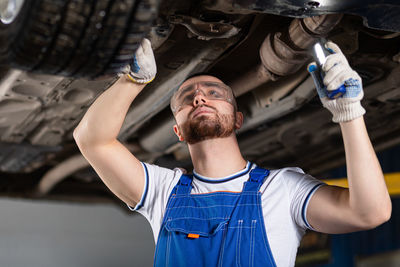 A young man auto mechanic in overalls at his workplace repairs the car's suspension