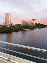 City by river against sky during sunset