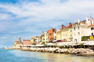 Buildings at waterfront against cloudy sky