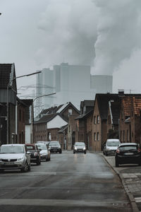 Cars on road by buildings in city against sky