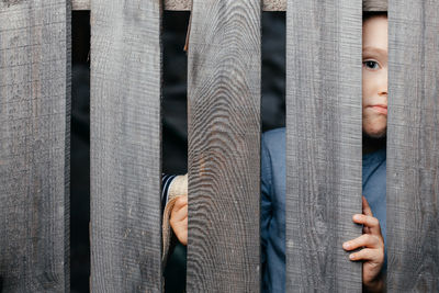 Happy smiling white boy looks out of the crack of a wooden fence. childish curiosity. espionage. 