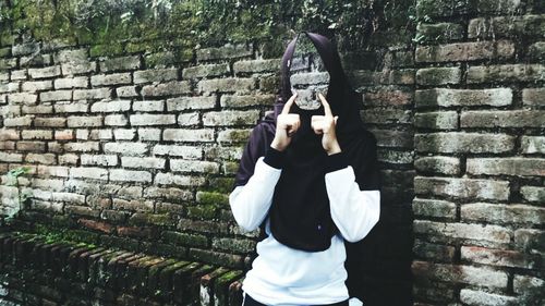 Digital composite image of woman gesturing against old brick wall