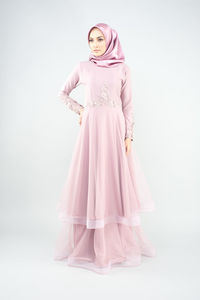 Full length portrait of woman standing against pink background