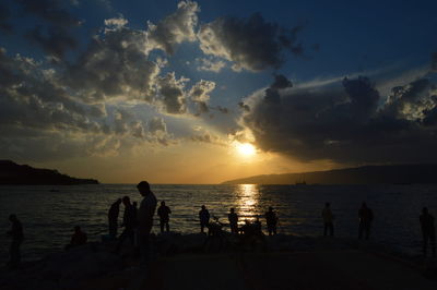 Silhouette people on beach against sky during sunset