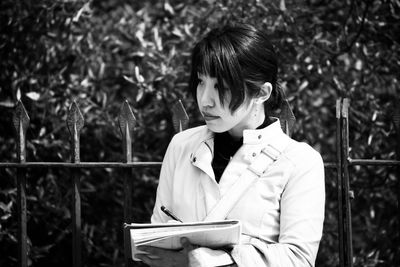 Young woman reading book against tree