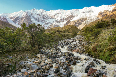 Scenic view of stream amidst snowcapped mountains against sky