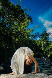 Side view of flexible woman bending over backwards on rock in forest