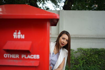 Portrait of woman hiding behind red mailbox