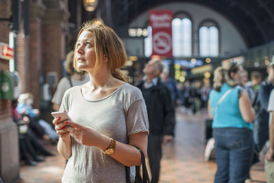 Mid adult woman with mobile phone looking up while standing on railway station