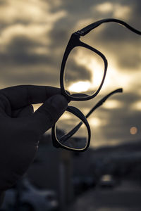 Cropped hand of person holding eyeglasses against sky