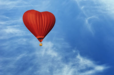 Red air balloon in the shape of heart against blue sky in a sunny bright day fly high above the tree
