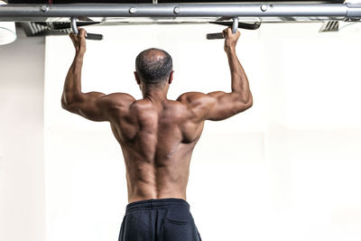 Rear view of shirtless man exercising in gym