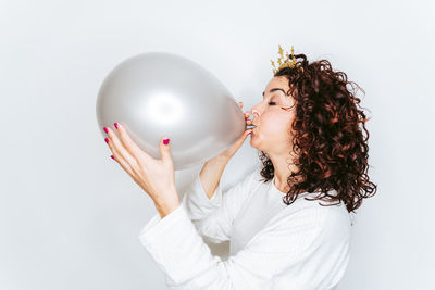 Woman blowing balloon while standing against white backgrounds