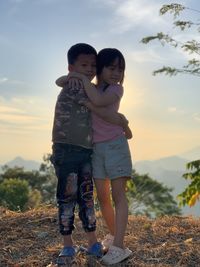 Side view of boy standing on rock against sky during sunset