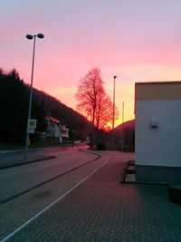 Empty road by buildings against sky at sunset