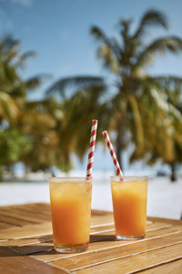 Two refreshing cold drinks on white sand beach. glasses of cocktails with drinking straws on table.