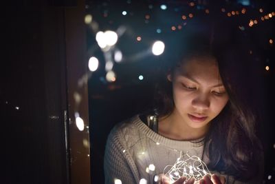 Teenage girl looking down while holding illuminated string lights