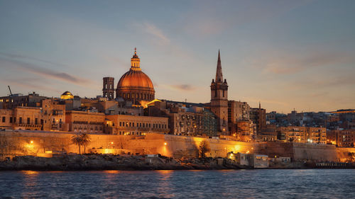 Illuminated buildings against sky during sunset in city