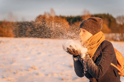 A woman blows a handful of snow from her hands at sunset in the evening