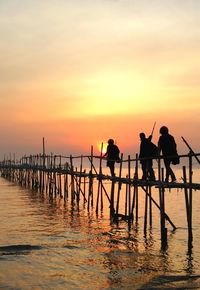 Silhouette men walking on pier over sea at sunset