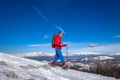 Rear view of man skiing on snowcapped mountain against blue sky