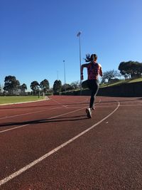 Rear view of woman running in sports track against clear blue sky