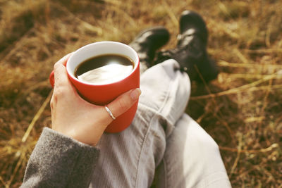 Low section of man holding coffee cup while sitting on grassy field