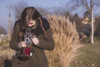 Young woman photographing through camera on field