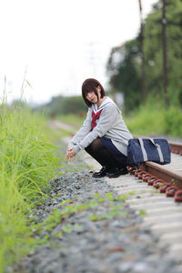 Portrait of young woman in school uniform sitting on railroad track