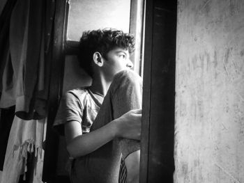 Thoughtful boy sitting on window at home