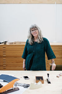 Portrait of smiling mature businesswoman standing at table in office