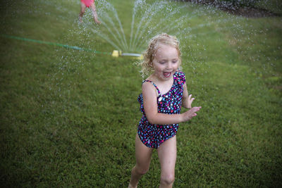 Girl playing with water on grassy field at backyard