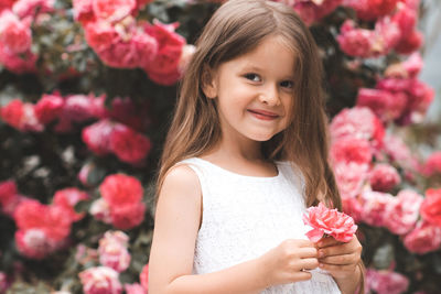 Cute baby girl 5-6 year old hold rose flower sit over bloom bushes in garden outdoor. spring season