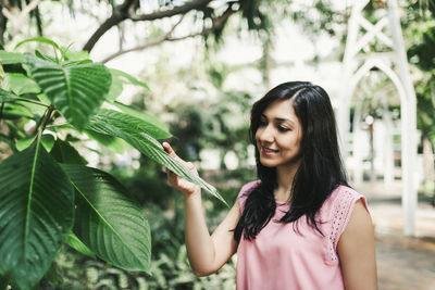 Happy young woman holding plant against trees