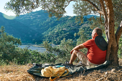 Side view of tourist man resting in olive grove, enjoying mountain view. hiking, healthy lifestyle.