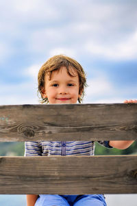 Portrait of smiling boy holding umbrella against sky