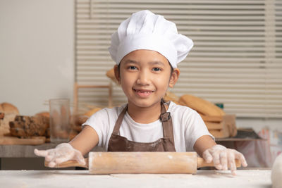 Asian little girl uses a rolling pin to knead the dough to make a homemade bakery.