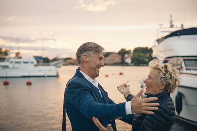 Side view of excited senior woman embracing man at harbor