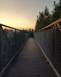 People walking on footbridge against sky during sunset