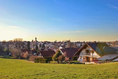 Scenic view of field by houses against sky