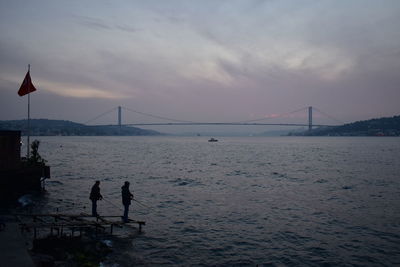 Suspension bridge silhouette and fishermen over the sea at sunset