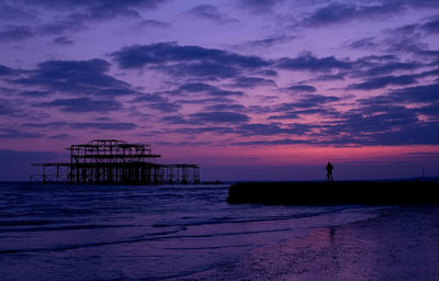 Silhouette person standing on rock formation by west pier during sunset