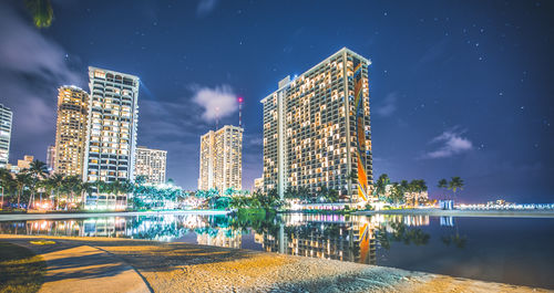 Illuminated modern buildings by reflecting pool against star field