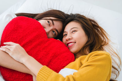 Women holding stuffed heart shape while lying on bed at home