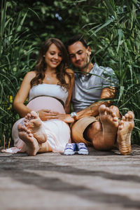 Husband and pregnant wife sitting with shoes amidst plants