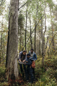 Mother showing bark of tree to son while exploring forest during vacation