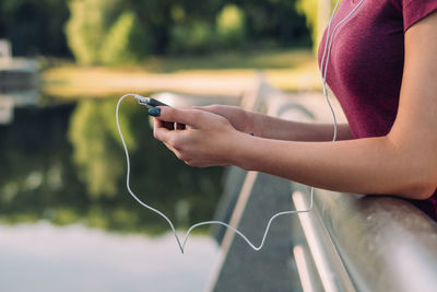 Midsection of woman listening music while standing on bridge