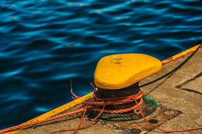 High angle view of ropes tied on yellow bollard by sea