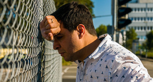 Depressed man standing by chainlink fence