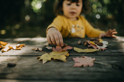 Close-up of child playing with maple leaves fallen on wood during autumn